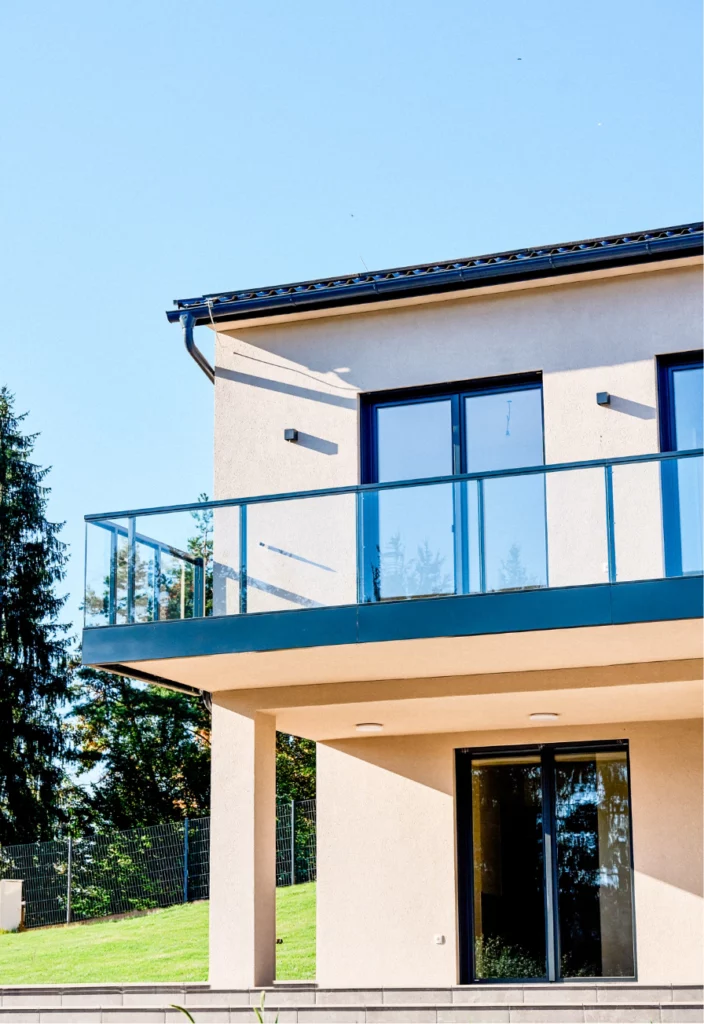 Moderne Hausfassade mit Glasbalkon, großer Terrasse und Blick ins Grüne.