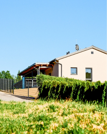 Außenansicht eines Einfamilienhauses mit Carport, Zaun und Grüneinfassung.